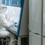 Scientist in protective gear working with laboratory equipment in a controlled environment.